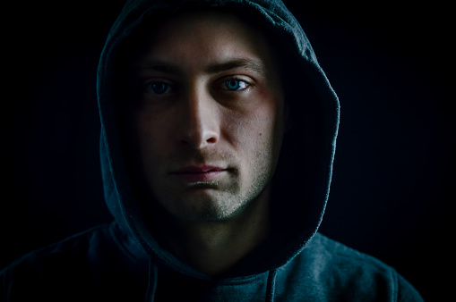 Portrait of a young man with a hood on his head looking grumpy in a dark atmosphere