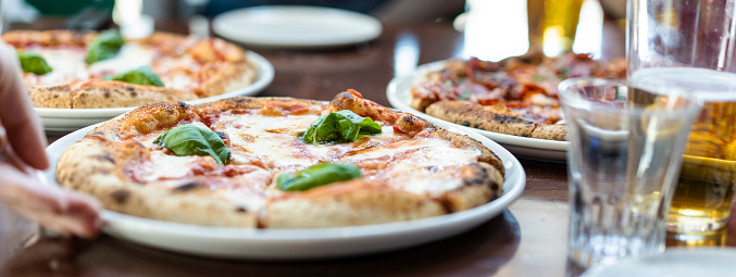 Horizontal banner or header with close up view of a Margherita Neapolitan style pizza with buffalo mozzarella, tomato sauce and basil - Waiter hand serving pizza at pizza restaurant