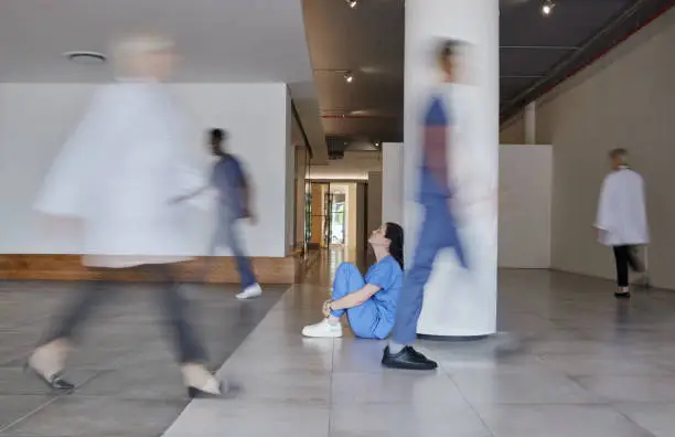 Photo of Shot of a young female doctor looking tired while working in a busy hospital