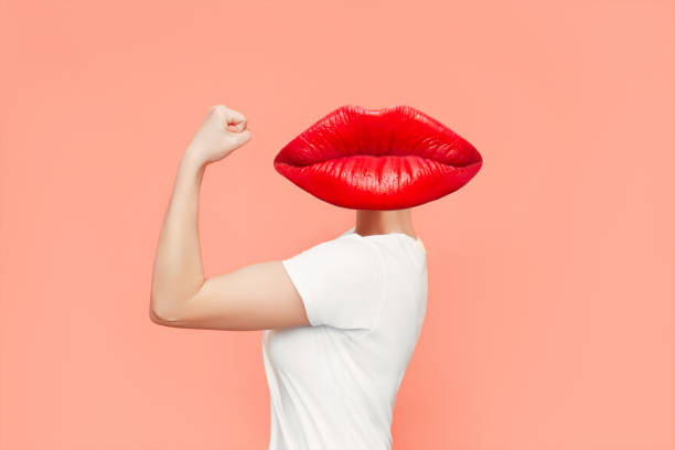 strong woman headed by red lips raises arm and shows bicep isolated on coral color background - muscular build bicep women female imagens e fotografias de stock