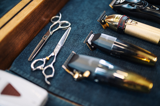 Hairdressing scissors and clippers lined up on worktop in Barber shop.