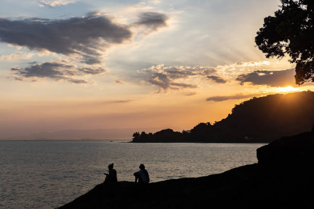 Beautiful sunset on the beach including the silhouette of some people looking at the horizon, clouds, sea and a colorful sky. Relaxing place for leisure, vacation and sightseeing.