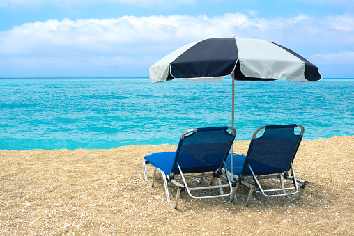 Empty Beach with two lounge chairs and beach umbrella. Azure blue water and amazing sky, Lefkada, Greece.