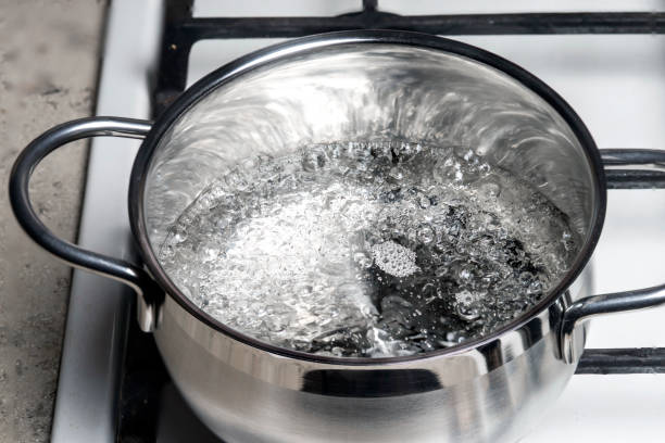 물은 가스 렌지의 스테인레스 스틸 팬에서 끓습니다. - 끓는 물에 삶기 뉴스 사진 이미지