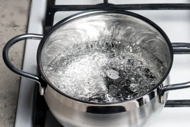 Photo of Water boils in a stainless steel pan on a gas stove.