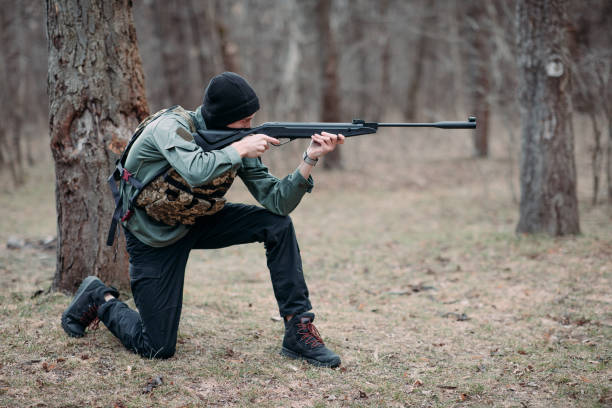 istock Young man aims from pump gun weared in body armor and balaclava. 1390102678