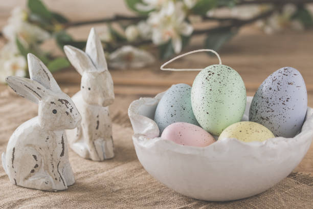 istock Decorative Easter eggs in pastel colors in a white handmade bowl and two wooden Easter bunnies on a wooden table 1390103038