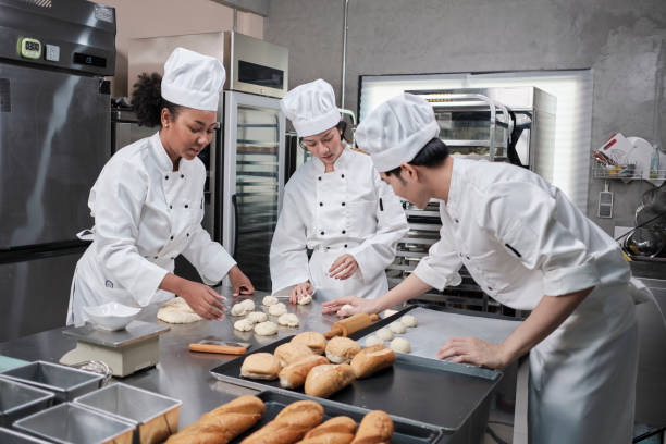 Chefs team in uniforms prepare to bake bread and pastry in stainless kitchen. stock photo