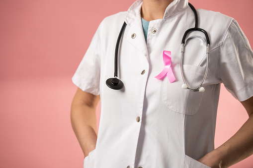 Unrecognizable female doctor wearing pink breast cancer awareness ribbon on white medical uniform.