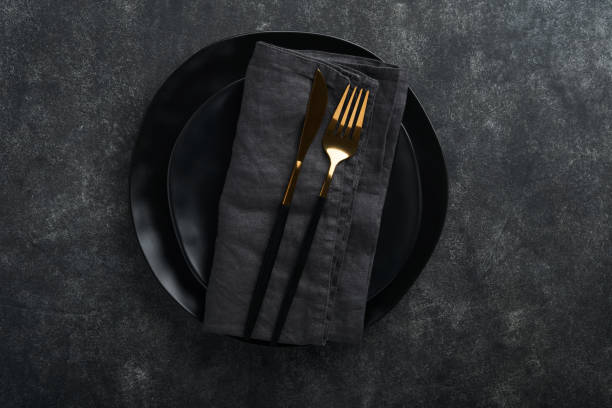 istock Ceramic empty black plate, silverware and linen kitchen towel napkin on old black ceramic cement concrete table background. Cooking stone backdrop. Top view with copy space. Flat lay 1390105702