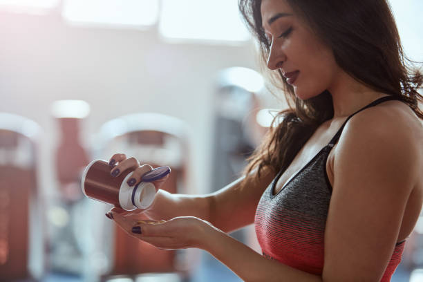 A fit sportswoman standing in a gym and taking pre workout pills. stock photo