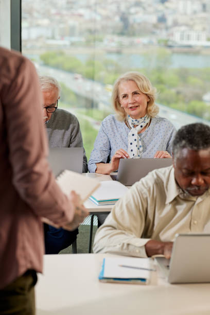 istock A senior woman is asking for an explanation in the computer course while sitting with elderly students in the classroom. 1390106413