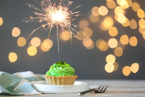 istock Cupcake with burning sparkler on table against blurred festive lights. Space for text 1390106418