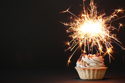 Cupcake with burning sparklers on black background. Space for text