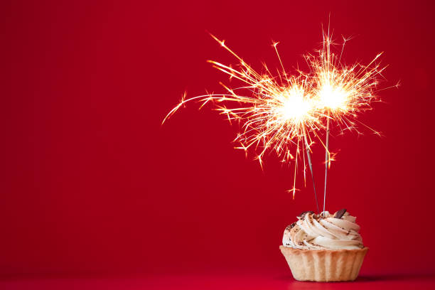 istock Cupcake with burning sparkler on red background. Space for text 1390106499
