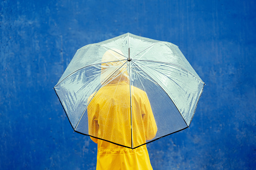 Horizontal rear view of person outdoors holding umbrella on blue background. Weather concept