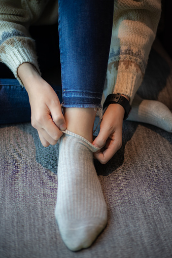 Close-up of a woman's hand in a sweater and jeans wearing gray socks on the sofa
