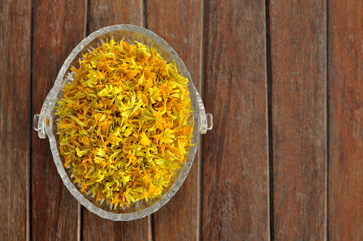 Yellow marigold petal, Tagetes, herbal infusion, herbal tea, Tisanes, Almost dry marigold petal for making herbal tea in glass bowl on the wood table.
