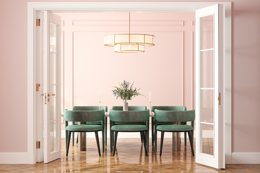Entrada de comedor con mesa de comedor, sillas de terciopelo verde y pared rosa al fondo photo