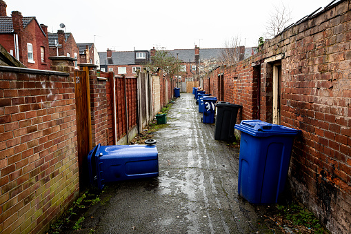 The backstreet of rows of terraced houses in a run down city in Northern England with wheelie bins left out for roadside collection with copy space