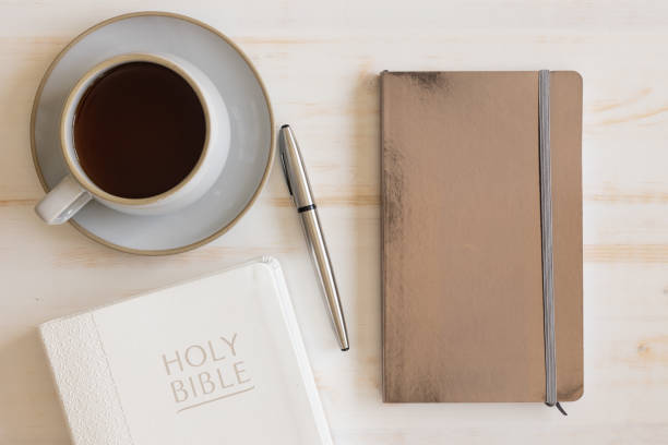 istock Cup of Coffee, bible and silver journal with pen on a white table 1390111753