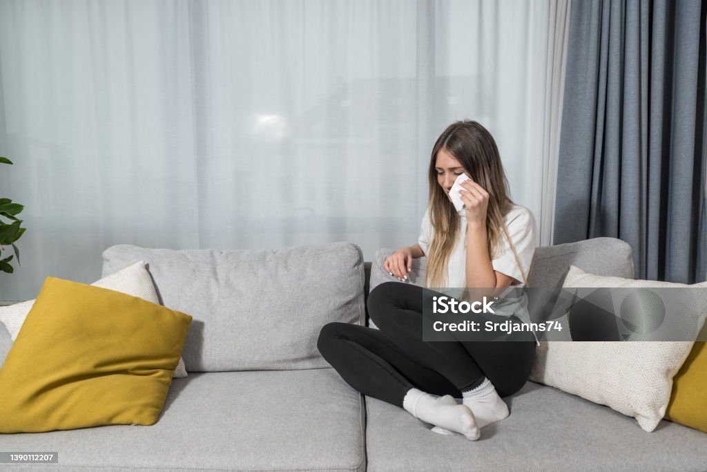 Depressed young woman covering face by hands, crying alone at home, upset girl sitting on sofa, feeling unhappy after quarrel or breakup, despair and lonely, psychological problem concept Crying Stock Photo