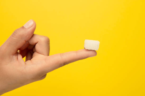 Sugar On The Finger Sugar cube on the finger, yellow background. sugar cube stock pictures, royalty-free photos & images