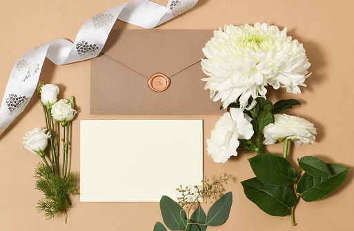 Beautiful arrangement of empty card, envelope, ribbon and white flowers flowers