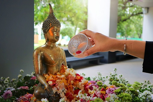 Woman's hand sprinkle water onto a Buddha image, a gesture of worship during the annual Songkran festival. Religion and holiday concept.