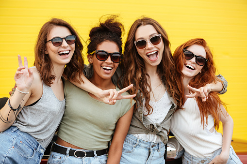 Image of four young happy women friends standing over yellow wall. Looking at camera.