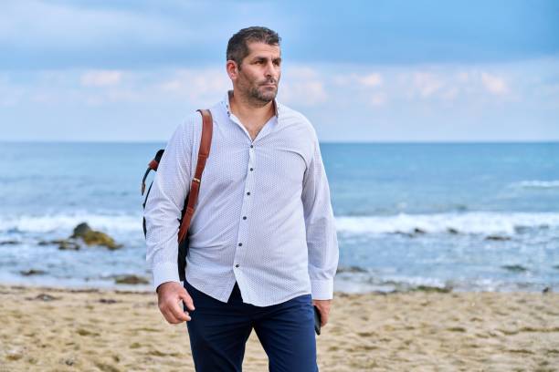 istock Serious confident successful mature man walking along the beach. 1390118021