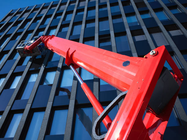 Cleaner workers use a cherry picker to clean a glass facade that reflects the blue sky. stock photo