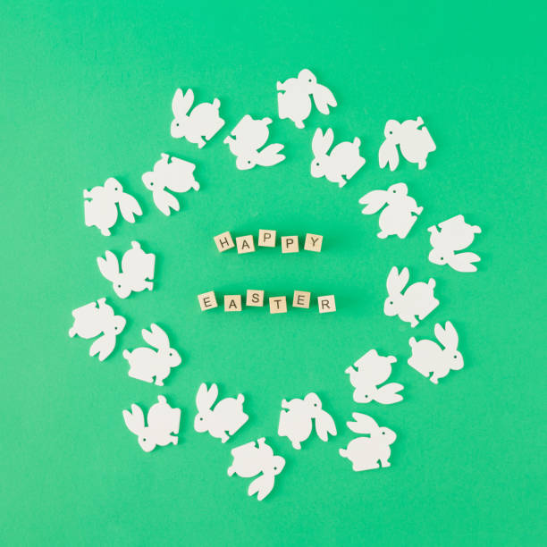 A creative arrangement made of white rabbits arranged in a circle shape within which the inscription is Happy Easter. Minimal flat lay concept.