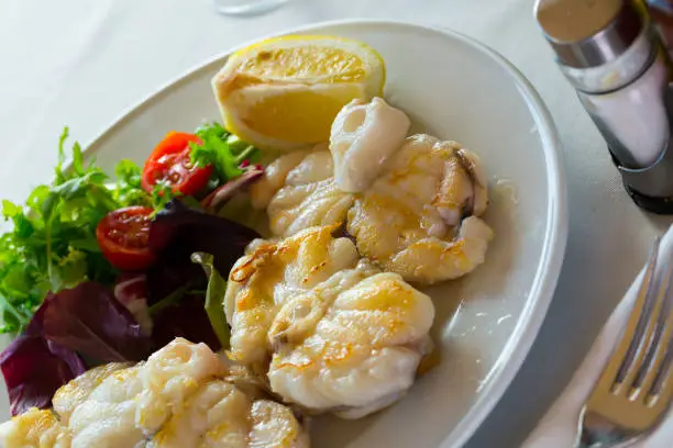 Seafood dish. Delicious grilled monkfish garnished with fresh greens, cherry tomatoes and lemon