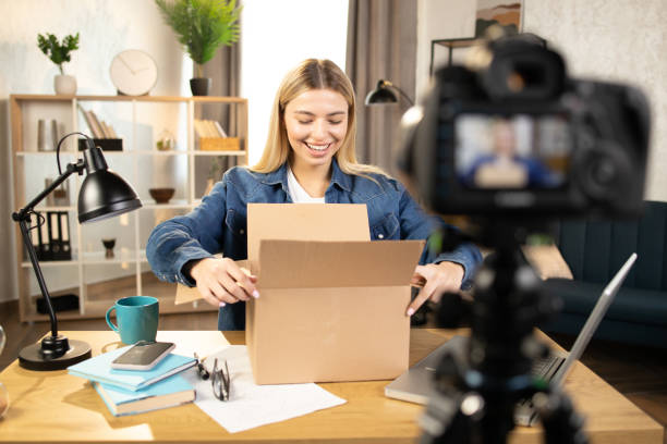 istock Blond pretty woman doing live stream while unpacking parcel 1390131393