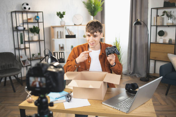 Man recording video while unpacking box with joystick Likable Caucasian man in casual wear taking wireless joystick for games from paper box while filming video on digital camera. Concept of technology and blogging. home recording studio setup stock pictures, royalty-free photos & images