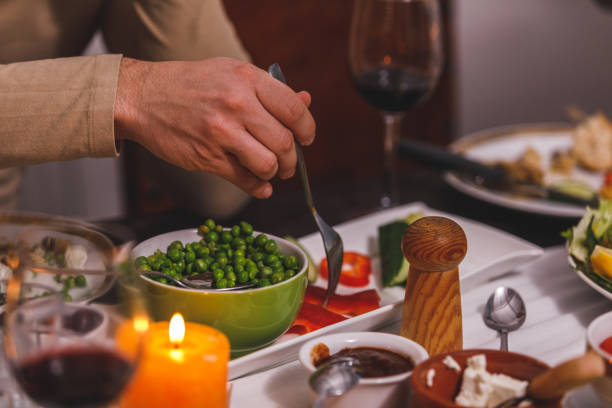 Close up shot of unrecognizable man taking sides from a platter while filling his plate with food during dinner party. Part of a series.