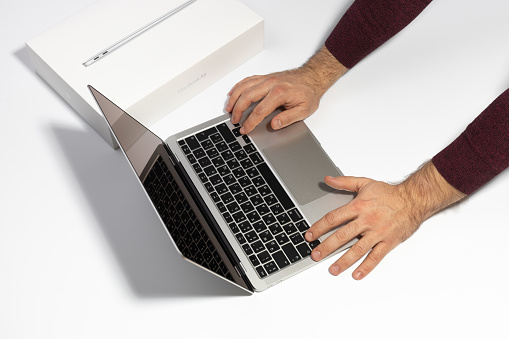 Saratov, Russia - February 26, 2022: man press key on Macbook Air 13 inch with M1 processor. Unpacking new Apple laptop closeup, white background. Advertising of modern technology and portable device.