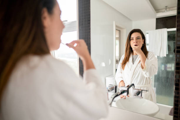 woman brushing her teeth in her bathroom mirror - woman in mirror backview imagens e fotografias de stock