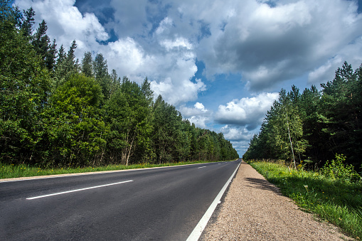 Low angle view of a straight two lane asphalt road with road marking goes through the forest