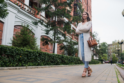 Confidence beautiful woman in casual clothes stands with crossed arms on the street and looks forward