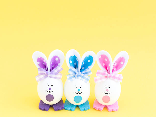 istock Three white creative eggs with painted eyes and multi-colored ears and paws on a yellow background in the center 1390147340