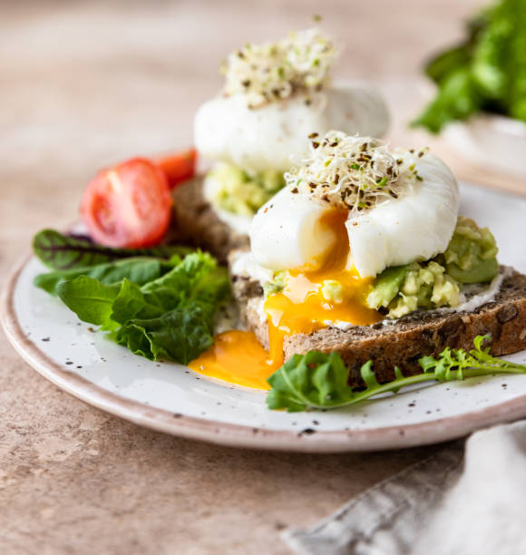 istock Sourdough bread with cream cheese, mashed avocado and poached egg served with salad leaves, tomatoes and sprouts. Healthy breakfast or brunch. Diet food concept. 1390147681