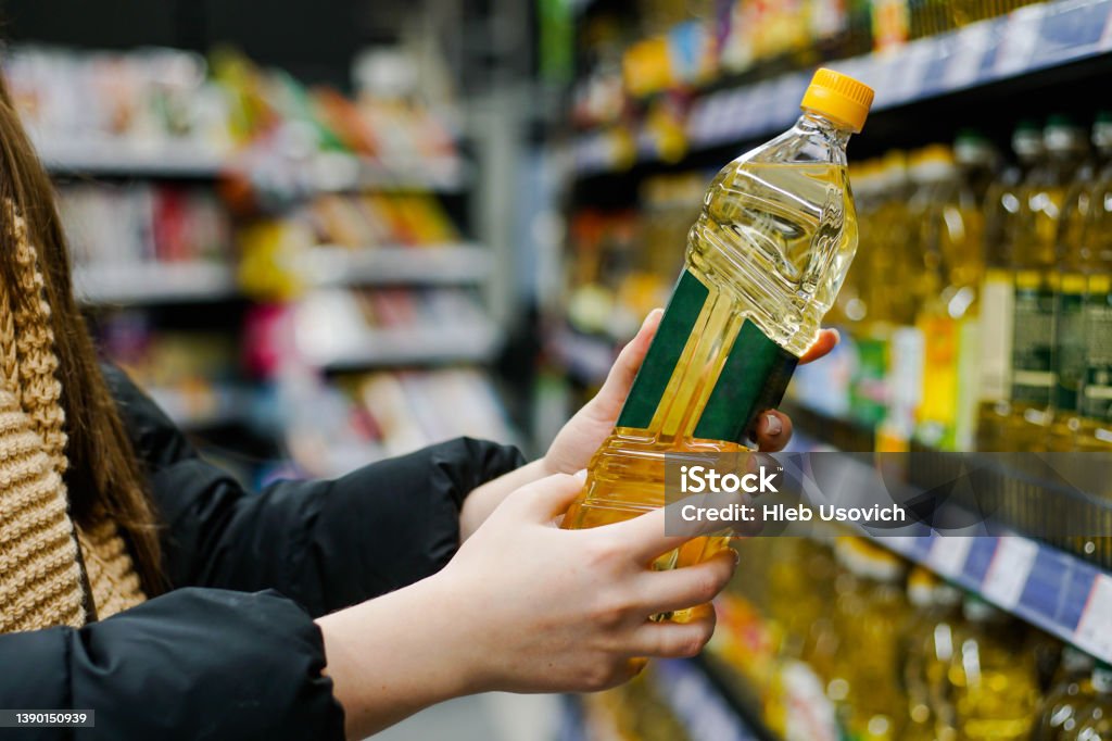 Woman choosing sunflower oil in the supermarket. Close up of hand holding bottle of oil at store. Cooking Oil Stock Photo