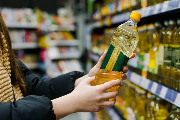 Photo of Woman choosing sunflower oil in the supermarket. Close up of hand holding bottle of oil at store.