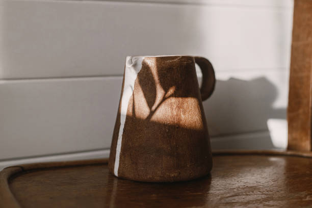 istock Home aesthetics. Modern ceramic kettle in sunlight on rustic wooden chair and leaves shadow. Stylish ceramic minimalist vase in sunny boho room with plants. 1390151374