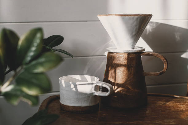 istock Morning coffee aesthetics. Modern ceramic cup, kettle and dripper for pour-over coffee in sunlight on rustic wooden chair and leaves shadow in stylish sunny room. Alternative coffee brewing method 1390151996