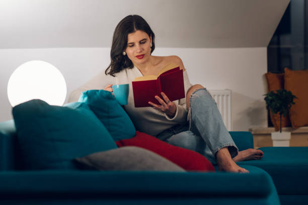 istock Woman reading a book and drinking tea while relaxing on a sofa at home 1390153158