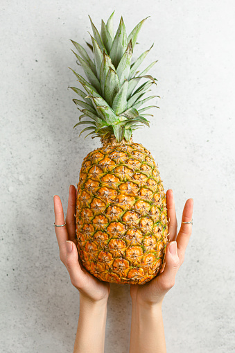 Woman's hand holding fresh ripe pineapple. Above.