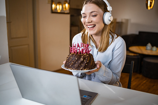 Woman is holding a birthday cake and communicating with the family online